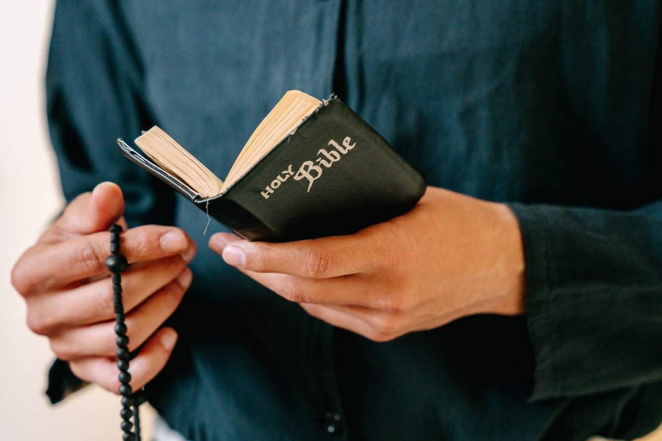 Hombre rezando con una biblia en su mano izquierda y un rosario en su mano derecha